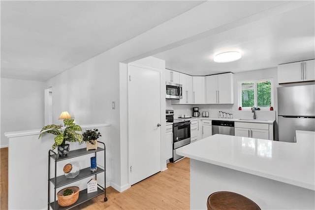 kitchen featuring kitchen peninsula, white cabinetry, light hardwood / wood-style flooring, and appliances with stainless steel finishes