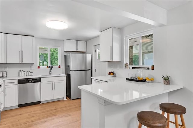 kitchen featuring kitchen peninsula, a kitchen breakfast bar, stainless steel appliances, and white cabinets