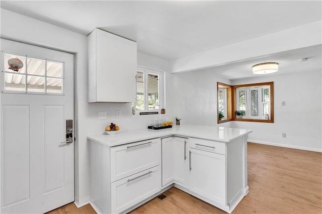 kitchen with light hardwood / wood-style floors, white cabinetry, kitchen peninsula, and a healthy amount of sunlight