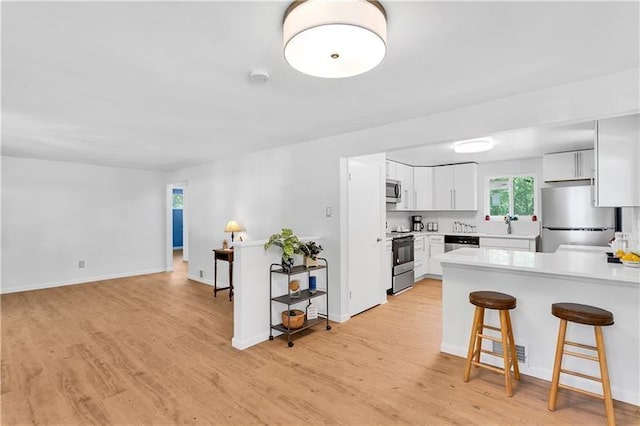 kitchen with a breakfast bar area, light hardwood / wood-style flooring, white cabinets, and appliances with stainless steel finishes