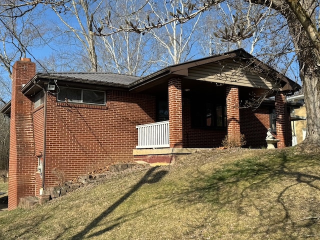 view of front of home with metal roof, brick siding, and a chimney