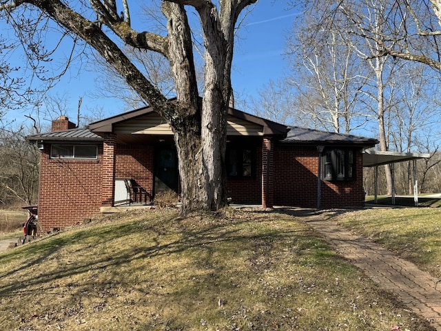 view of side of home featuring brick siding, an attached carport, a chimney, and a lawn