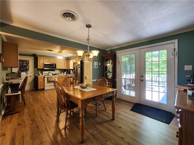 dining space featuring light wood-type flooring, a textured ceiling, french doors, and crown molding