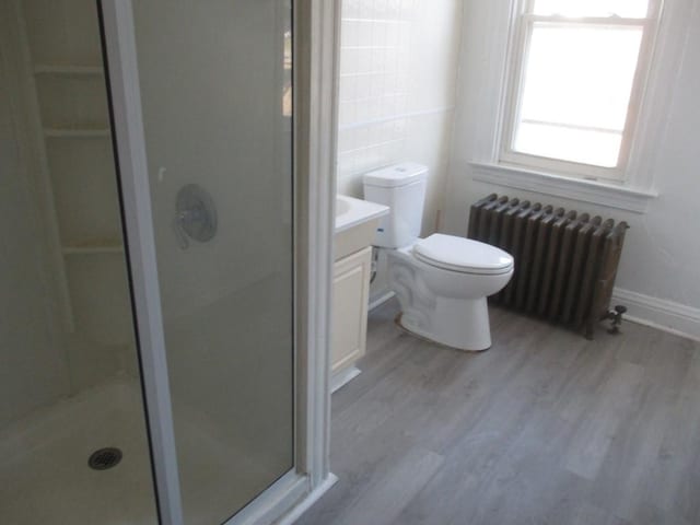 full bathroom featuring radiator, toilet, a stall shower, vanity, and wood finished floors