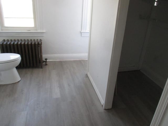 bathroom featuring radiator heating unit, wood finished floors, toilet, and baseboards