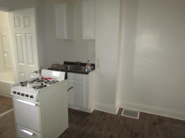 kitchen featuring visible vents, dark wood-type flooring, white cabinetry, baseboards, and white gas range oven