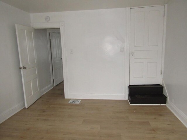 empty room with light wood-type flooring, visible vents, and baseboards