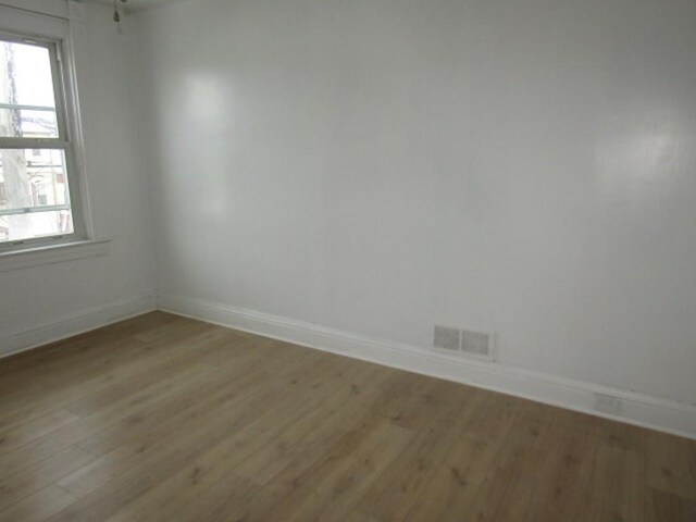 empty room featuring light wood-style floors, baseboards, and visible vents