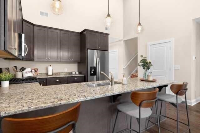 kitchen with light stone counters, sink, hanging light fixtures, stainless steel appliances, and a high ceiling