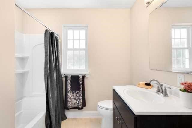 full bathroom with a healthy amount of sunlight, shower / bathtub combination with curtain, vanity, and toilet