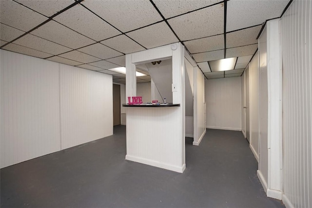 finished below grade area featuring a drop ceiling, baseboards, and a dry bar