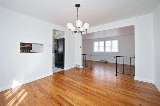 unfurnished room with visible vents, baseboards, a notable chandelier, and light wood-style flooring