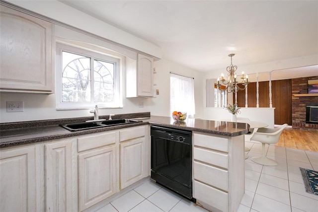 kitchen featuring a peninsula, a sink, black dishwasher, a brick fireplace, and a chandelier