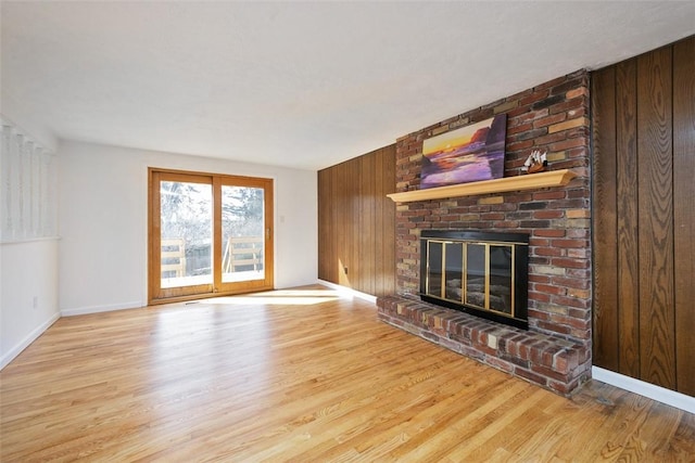 unfurnished living room featuring a fireplace, wooden walls, wood finished floors, and baseboards