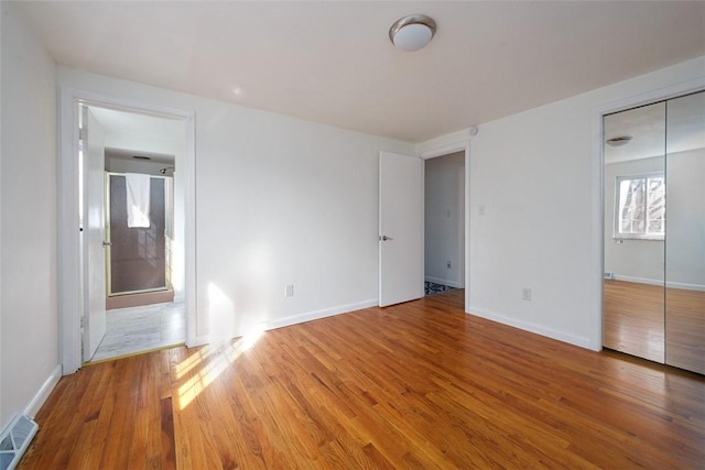 unfurnished bedroom featuring a closet, visible vents, baseboards, and wood finished floors