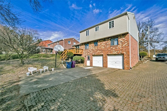 back of house featuring decorative driveway, brick siding, and an attached garage