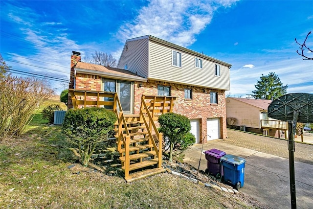 back of house with driveway, a chimney, stairs, a garage, and brick siding