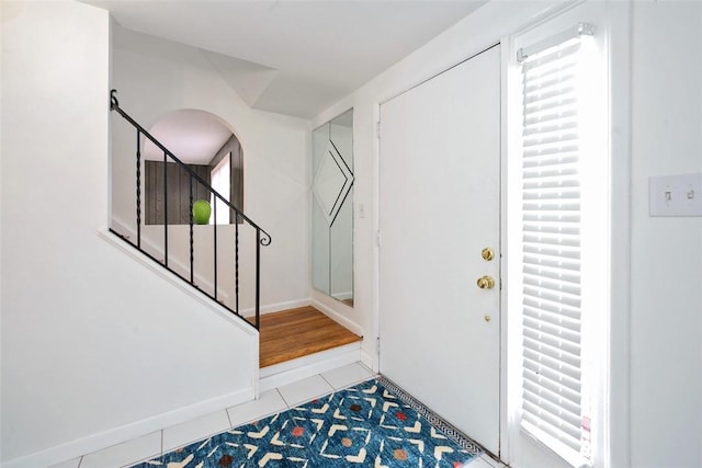 tiled foyer entrance with arched walkways, stairs, and baseboards