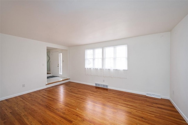 spare room with wood finished floors, visible vents, and baseboards