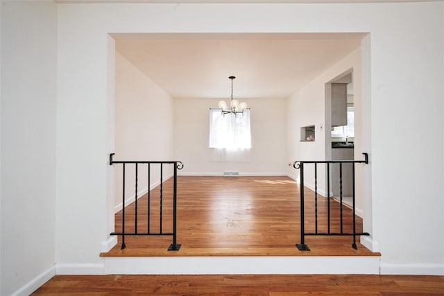 staircase with an inviting chandelier, wood finished floors, and baseboards