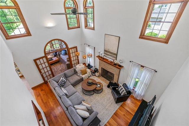 living room with a towering ceiling, a brick fireplace, wood-type flooring, and ceiling fan