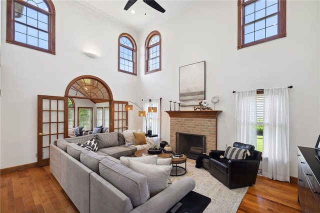 living room featuring a towering ceiling, a fireplace, wood-type flooring, and ceiling fan