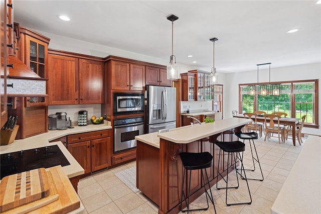 kitchen featuring decorative light fixtures, a kitchen island, stainless steel appliances, a kitchen bar, and light tile floors