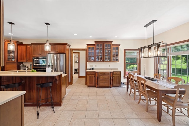 kitchen with a healthy amount of sunlight, light tile flooring, pendant lighting, and appliances with stainless steel finishes