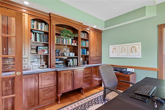 home office with built in desk, light hardwood / wood-style floors, and a textured ceiling