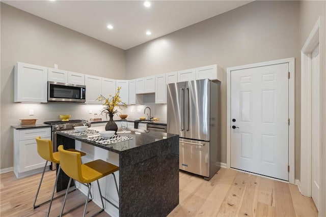 kitchen featuring a breakfast bar, a kitchen island, a towering ceiling, stainless steel appliances, and white cabinets