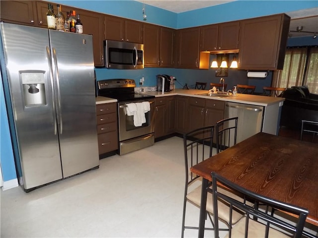 kitchen featuring appliances with stainless steel finishes, light countertops, dark brown cabinets, light floors, and a sink