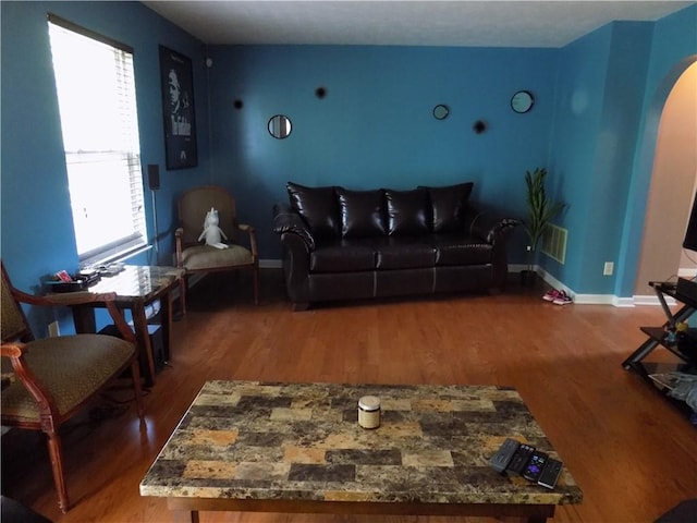 living room featuring arched walkways, baseboards, and wood finished floors