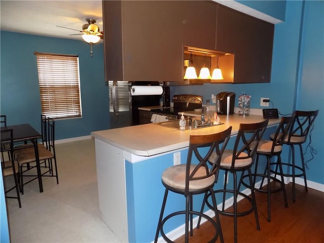 kitchen featuring a breakfast bar area, a peninsula, black / electric stove, light countertops, and a sink