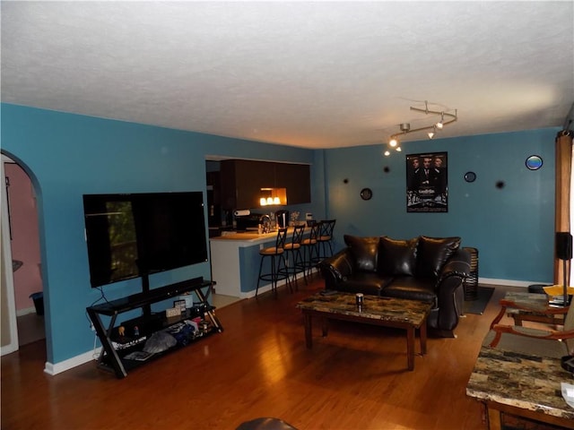 living room featuring arched walkways, dark wood finished floors, and baseboards