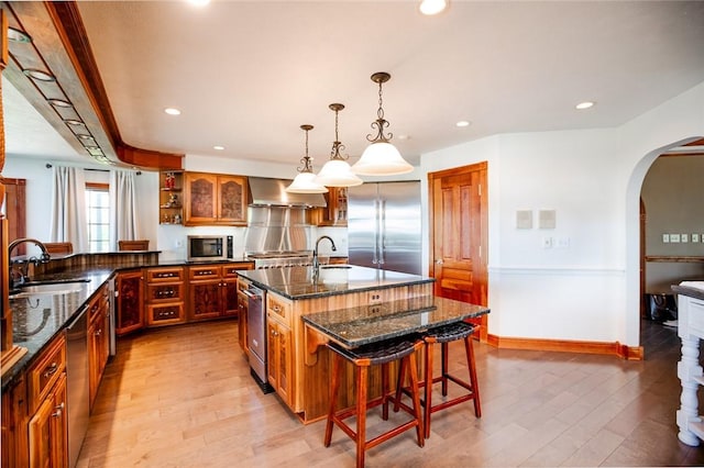 kitchen featuring light wood-style flooring, a sink, appliances with stainless steel finishes, arched walkways, and extractor fan