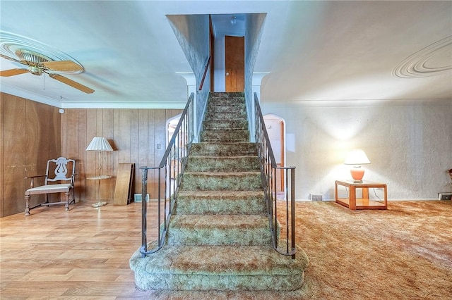 stairway featuring hardwood / wood-style floors, ceiling fan, crown molding, and wooden walls