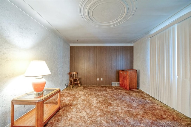 sitting room featuring carpet floors, wooden walls, and ornamental molding