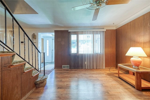 foyer featuring light wood-type flooring, ceiling fan, and wooden walls