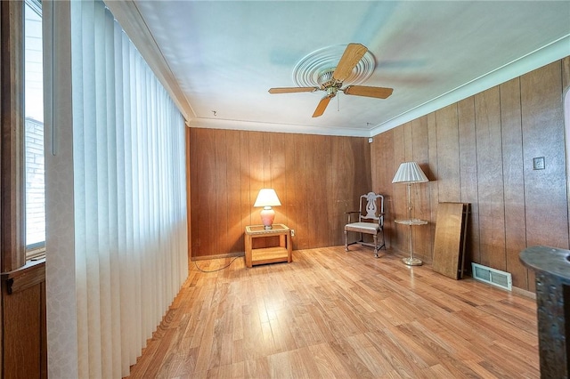 unfurnished room with ceiling fan, wooden walls, crown molding, and light wood-type flooring