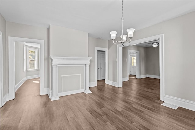 unfurnished dining area featuring ceiling fan with notable chandelier and dark hardwood / wood-style flooring