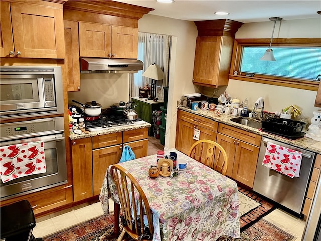 kitchen with light stone countertops, stainless steel appliances, pendant lighting, sink, and light tile floors