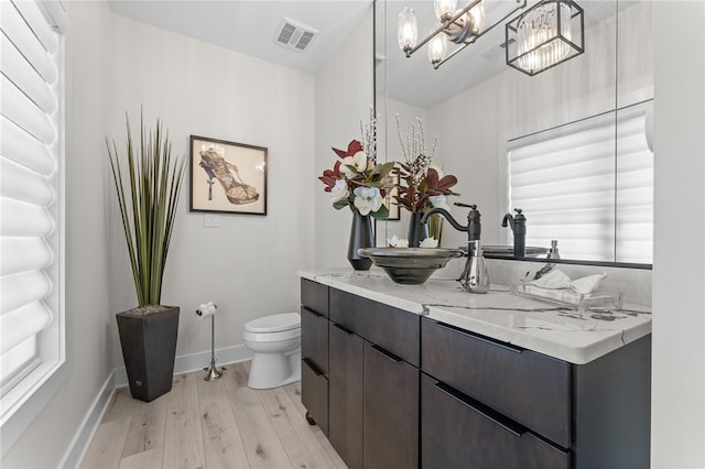 bathroom featuring a notable chandelier, a healthy amount of sunlight, toilet, hardwood / wood-style flooring, and vanity