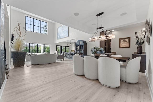 dining space featuring an inviting chandelier, a towering ceiling, light hardwood / wood-style flooring, and a tray ceiling