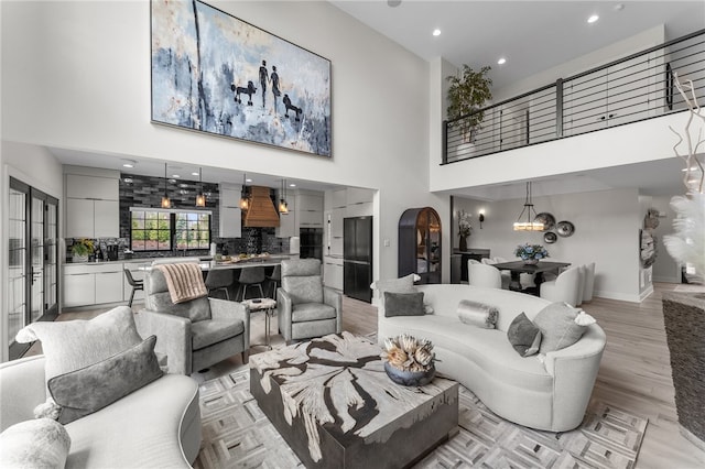 living room featuring a towering ceiling, light wood-type flooring, and an inviting chandelier