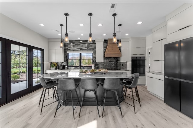 kitchen featuring light hardwood / wood-style floors, tasteful backsplash, custom exhaust hood, black appliances, and a kitchen island