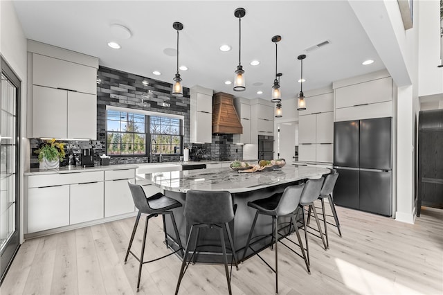 kitchen with custom range hood, a kitchen island, backsplash, light wood-type flooring, and pendant lighting