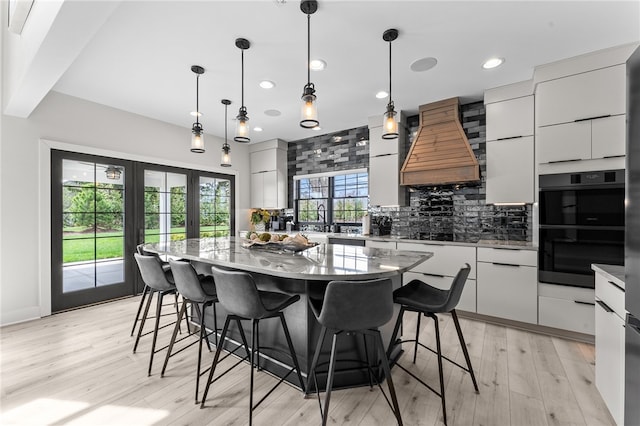 kitchen featuring tasteful backsplash, decorative light fixtures, custom range hood, a center island, and double oven