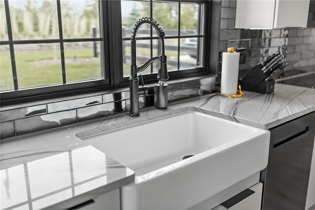 room details featuring tasteful backsplash, stainless steel dishwasher, light stone counters, sink, and white cabinets