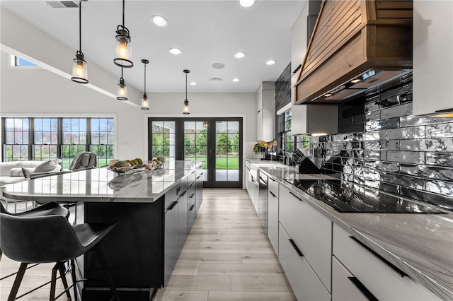 kitchen with light hardwood / wood-style floors, a kitchen island, tasteful backsplash, black electric cooktop, and pendant lighting