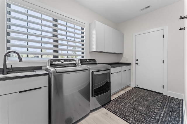 washroom with a wealth of natural light, cabinets, light hardwood / wood-style floors, and independent washer and dryer